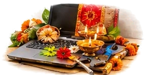 A laptop and work tools decorated with flowers and a red cloth, with lit diyas in front, as on Ayudha Puja