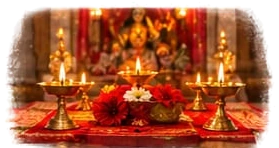 Rows of lit brass diyas and red flowers in front of the Devi at a temple shrine